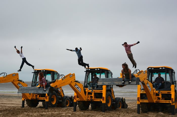 JCB on beach with people jumping